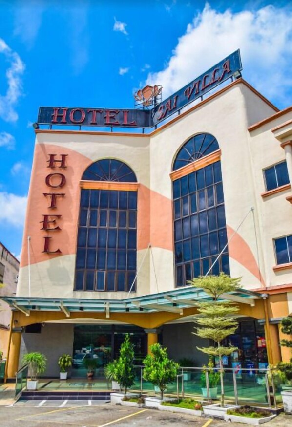A hotel with a prominent "HOTEL" sign, large arched windows, and a covered entrance area with potted plants. - Sai Villa Hotel (Nilai)