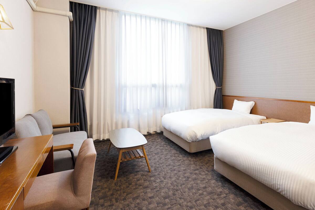 A hotel room with a TV, two beds, a desk, and a chair.