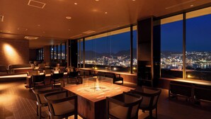 Ett modernt hotellrum med ett stort panoramafönster, en matplats med ett centralt placerat bord och en sittgrupp.