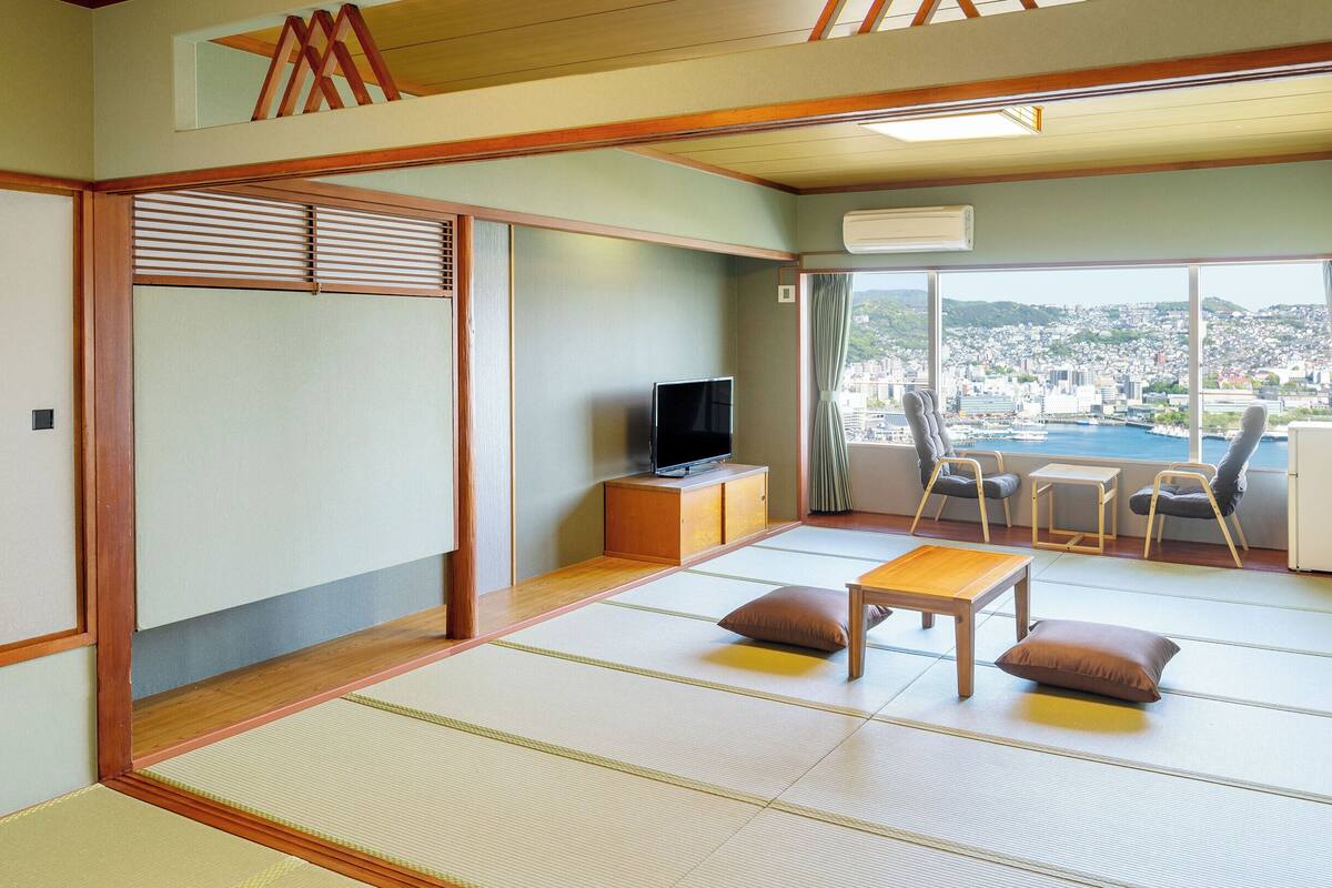 A traditional Japanese room with tatami flooring, a television, a small table, and a view of a cityscape.