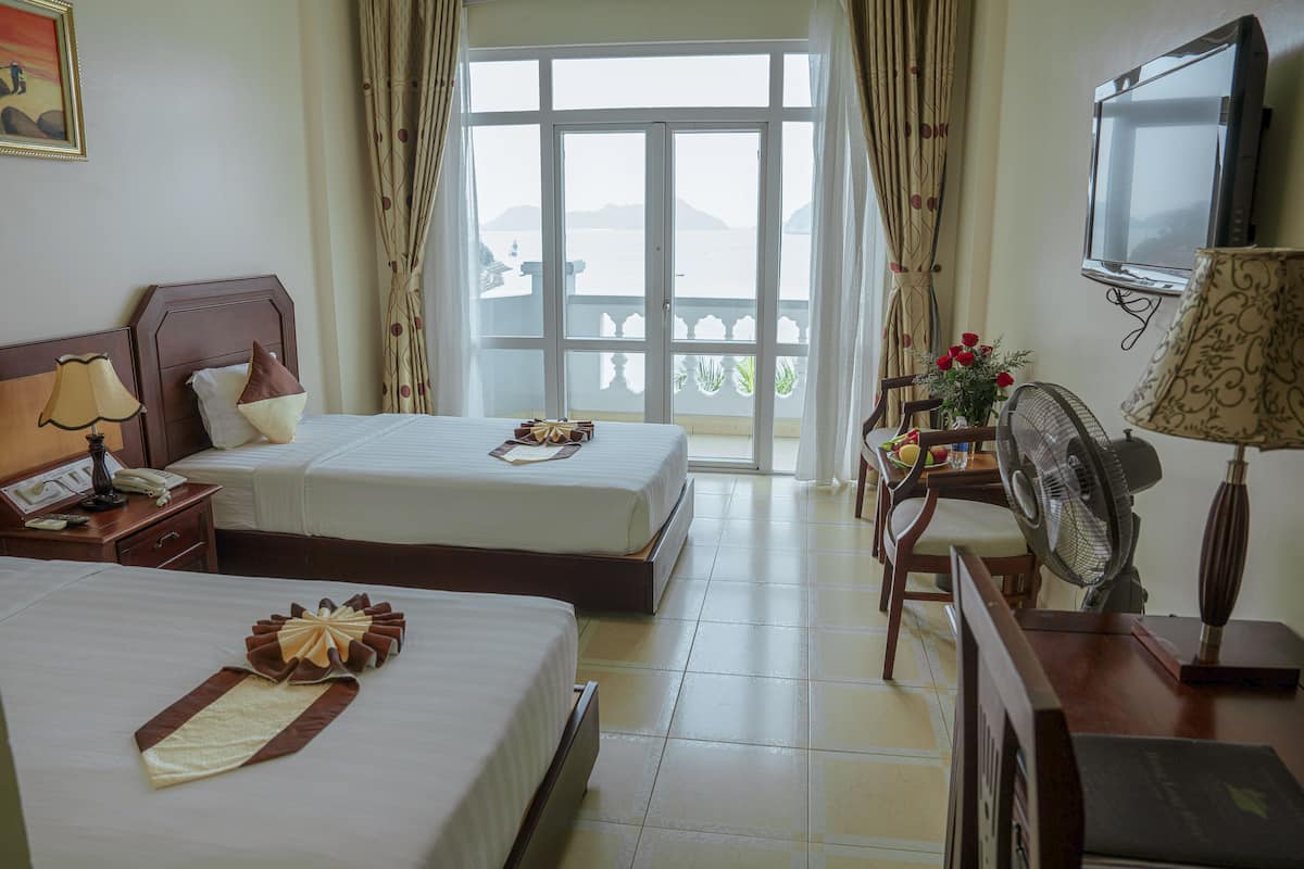 A hotel room with two beds, a TV, a fan, and a balcony with a view.