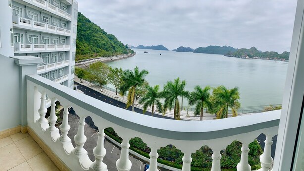 A balcony with a view of a calm body of water, a road, and a green hillside. - Hung Long Harbour Hotel (Hai Phong)