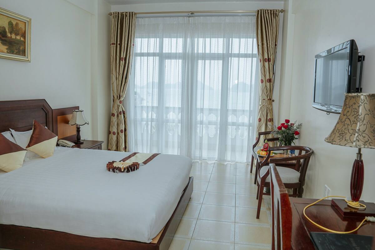 A hotel room with a large bed, a desk with a chair, a television, and a window with curtains.