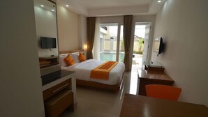 A hotel room with a bed, a desk, a chair, a TV, and a view of the outside. - Griya Sunset Kuta (Kuta)