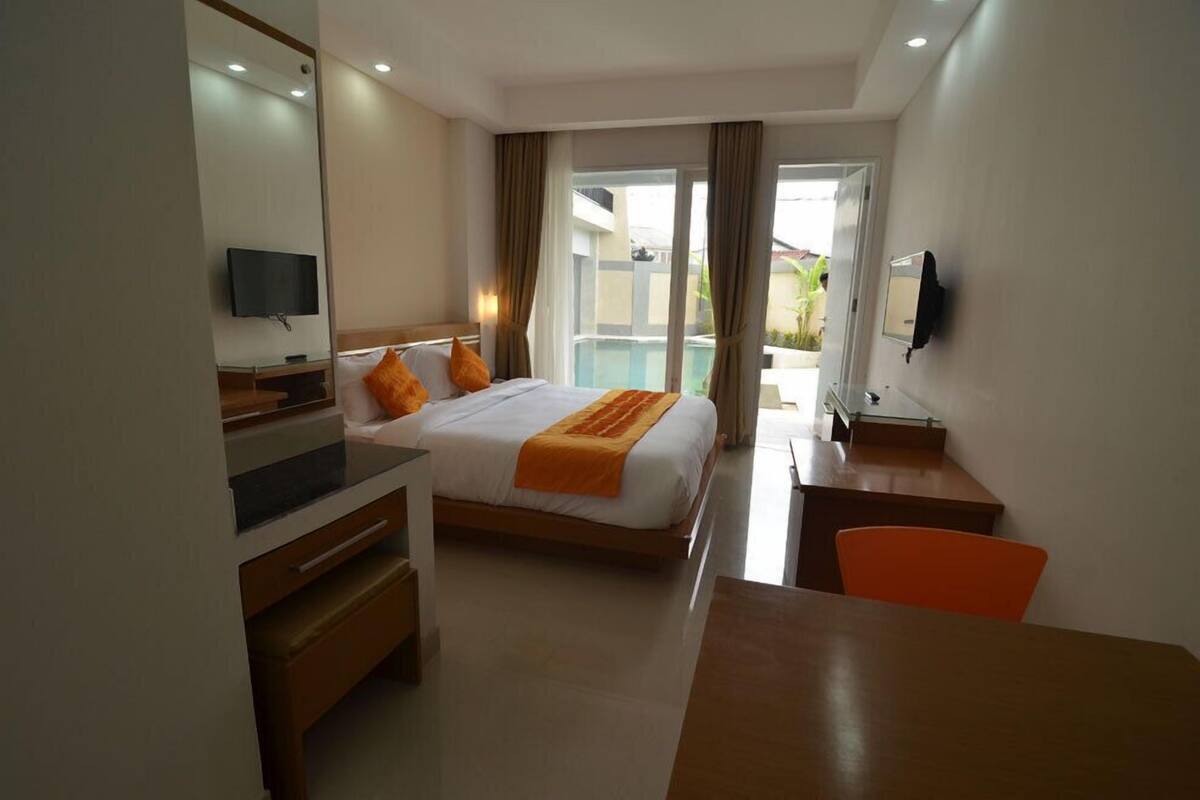 A hotel room with a bed, a desk, a chair, a TV, and a view of the outside.