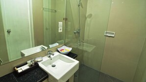 A modern bathroom with a glass-enclosed shower, a white sink, and a mirror. - Griya Sunset Kuta (Kuta)
