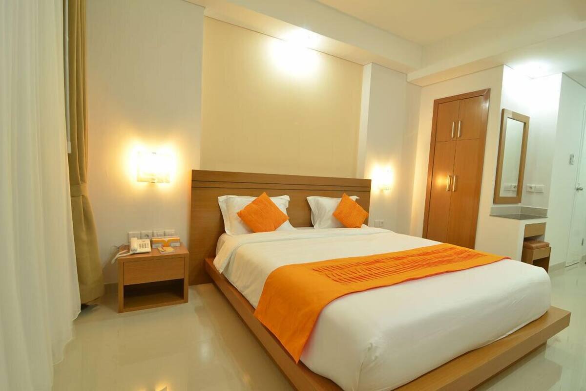 A hotel room with a large bed, two bedside tables, a nightstand, a mirror, and a wardrobe.