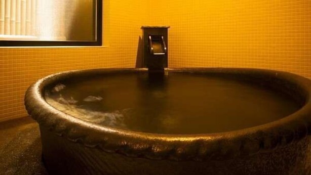A large, round hot tub with a faucet in a room with yellow tiled walls.