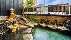 Een traditionele Japanse onsen met een stenen bad, houten banken en uitzicht op bergen.