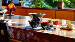 Een eetruimte met een gedekte tafel, een theepot en een raam met uitzicht op groen en gebouwen.