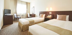 Quarto de hotel com duas camas, uma mesa, uma cadeira, uma televisão e um abajur.