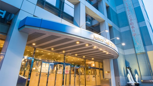 Una entrada de hotel moderna con fachada de vidrio, área de acceso cubierta y una señal que indica que es un hotel.