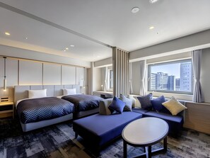 A modern hotel room with a large bed, a sofa, a small table, and a view of the city through the window.