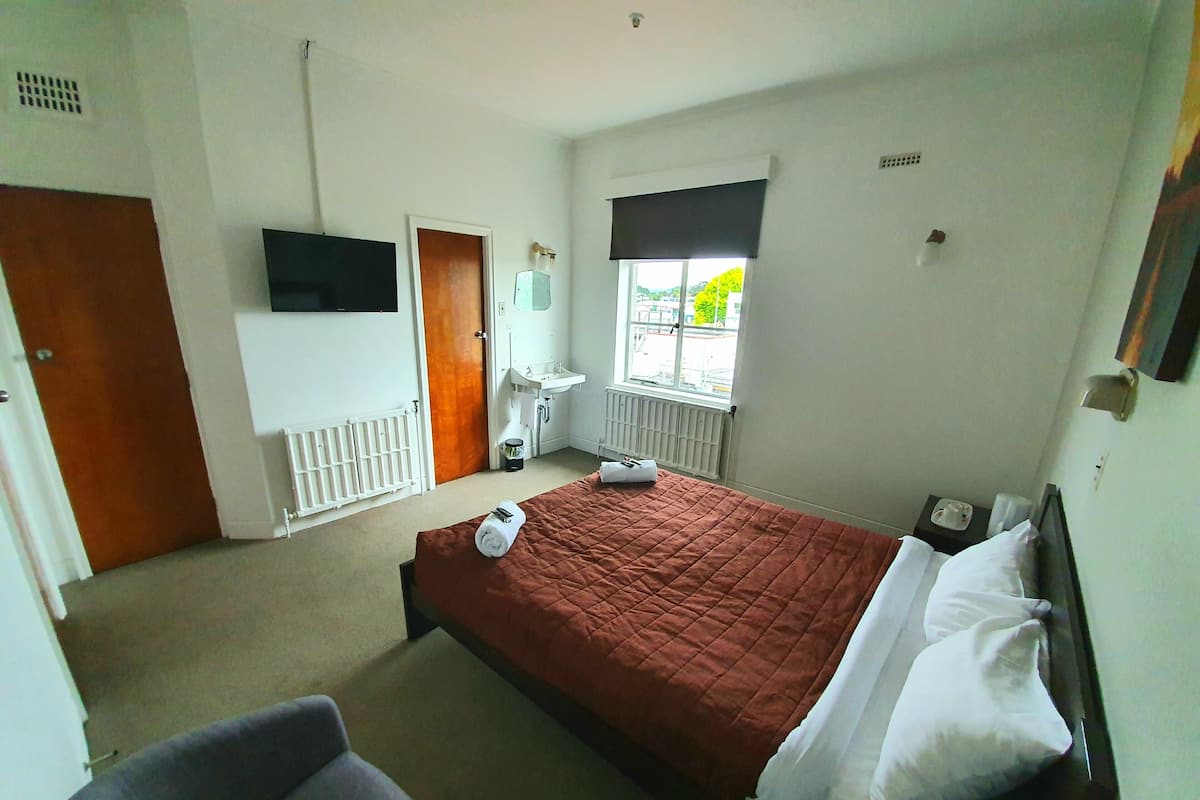 A hotel room with a bed, a chair, a TV, a window, and a bathroom.