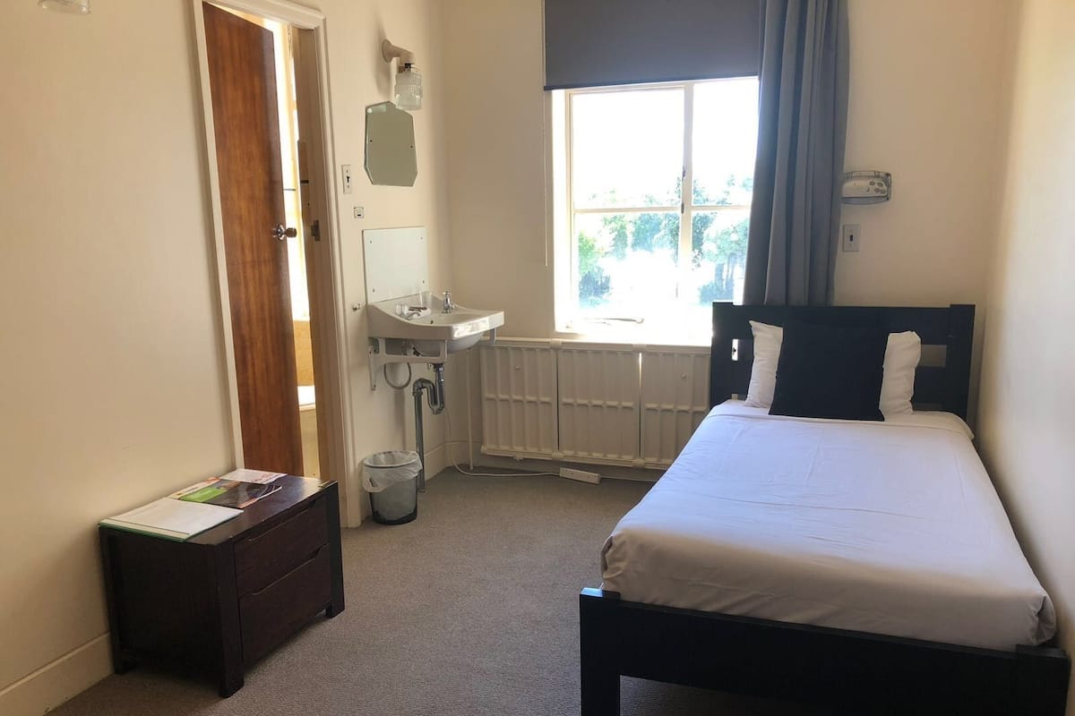 A bedroom with a bed, a window with a view, a sink, and a small trash bin.