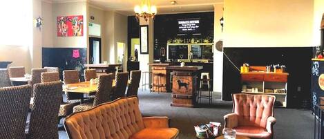Un vestíbulo amplio con zona de bar, asientos y una pantalla de televisión.