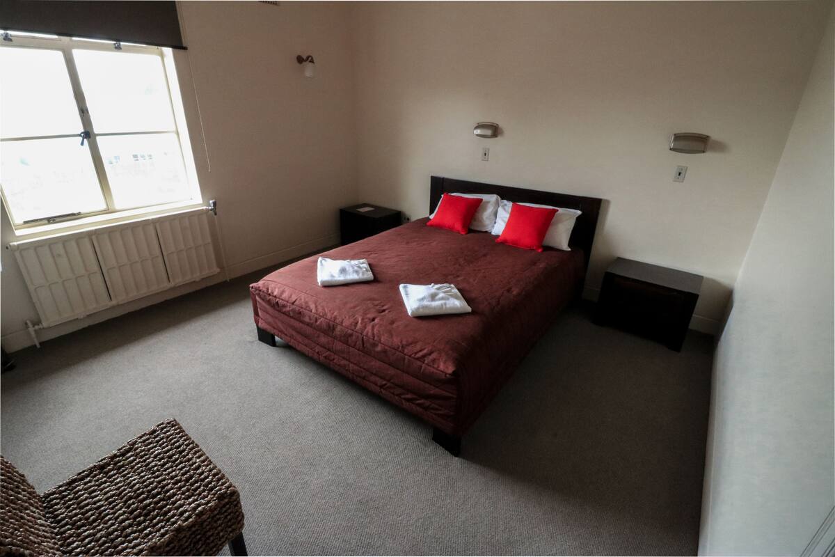 A bedroom with a large bed, a nightstand, a chair, and a window.