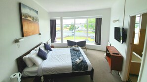 Une chambre d’hôtel avec un grand lit, un bureau, une chaise, une télévision et une fenêtre donnant sur un parking et des immeubles.