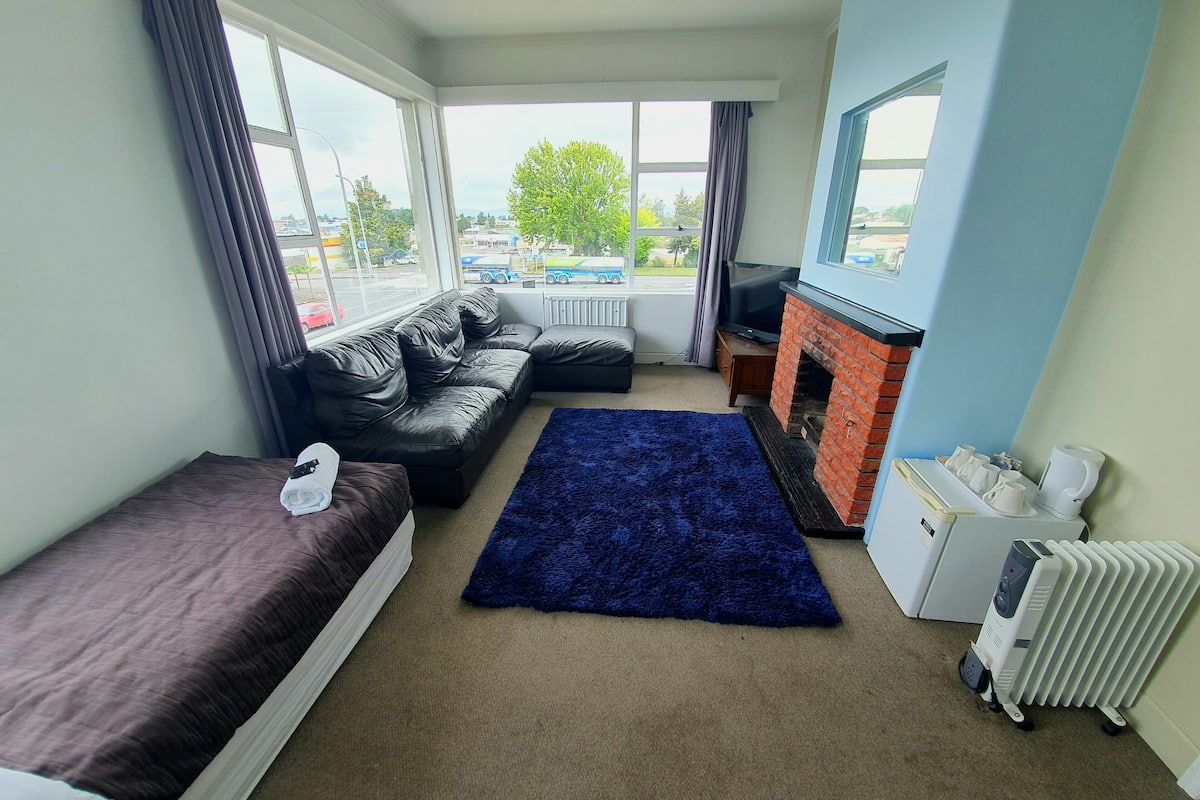 A room with a bed, a sofa, a blue rug, a fireplace, and a radiator.