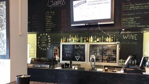Un espace bar avec un comptoir noir, un tableau affichant le menu et un assortiment de bouteilles.