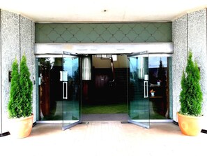 A hotel entrance with a glass door, a green patterned wall, and two potted plants. - Putaruru Hotel (Putaruru)
