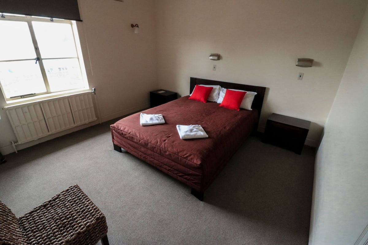 A bedroom with a large bed, a nightstand, a chair, a radiator, and a window.