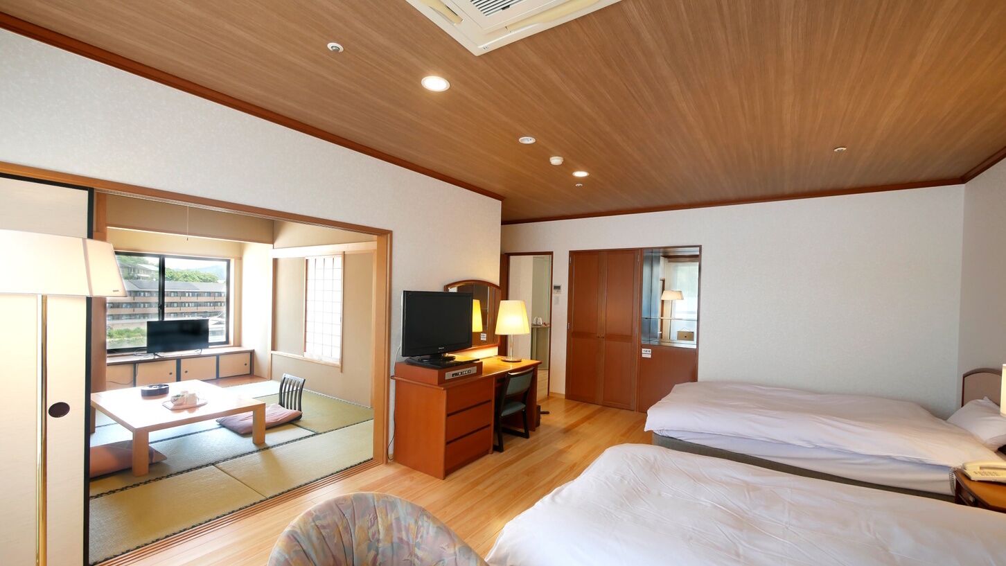 A hotel room with a wooden ceiling, a desk with a television, two beds, and a view through a sliding door.