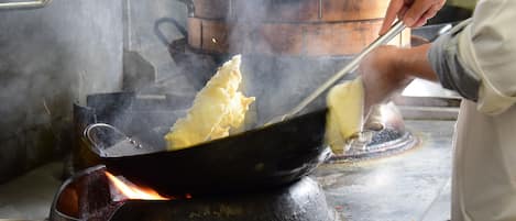 A person cooking in a wok on a stove, with steam rising and several metal bowls on the counter.