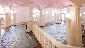 Een groot overdekt zwembad met meerdere kolommen en een witte balustrade.