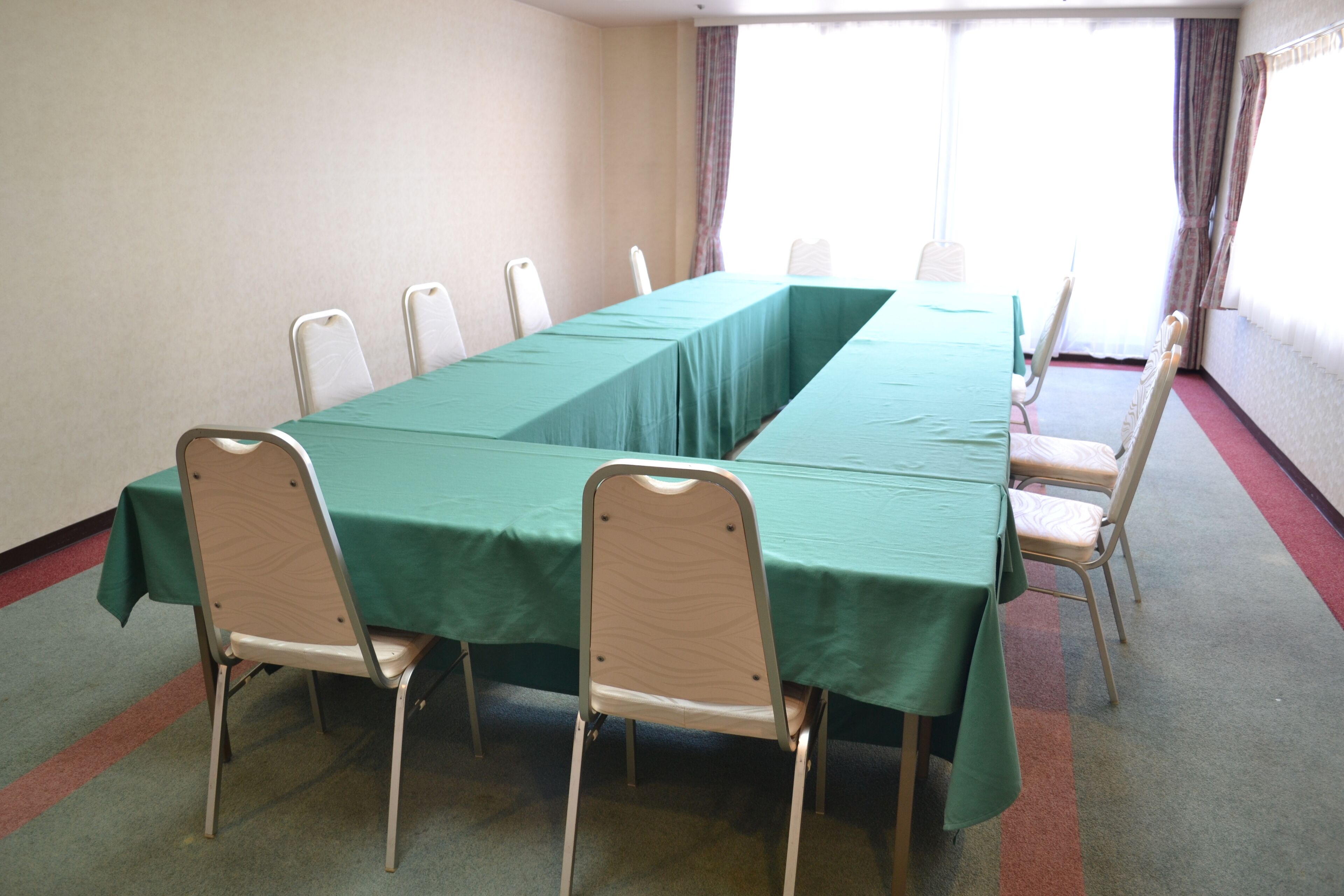 A conference room with a long table and chairs, carpeted floor, and large windows with curtains.