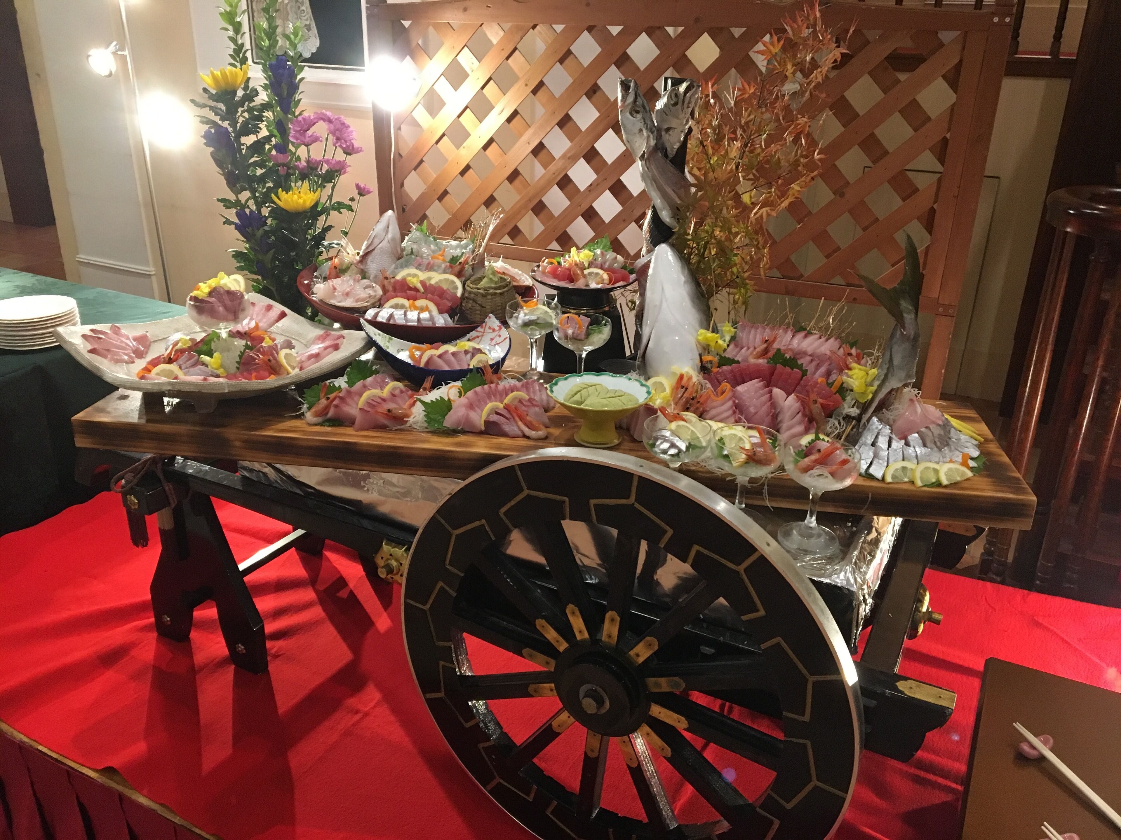 Una mesa de buffet con diversos platos, entre ellos mariscos y verduras, montada sobre un carrito de madera con una rueda grande.