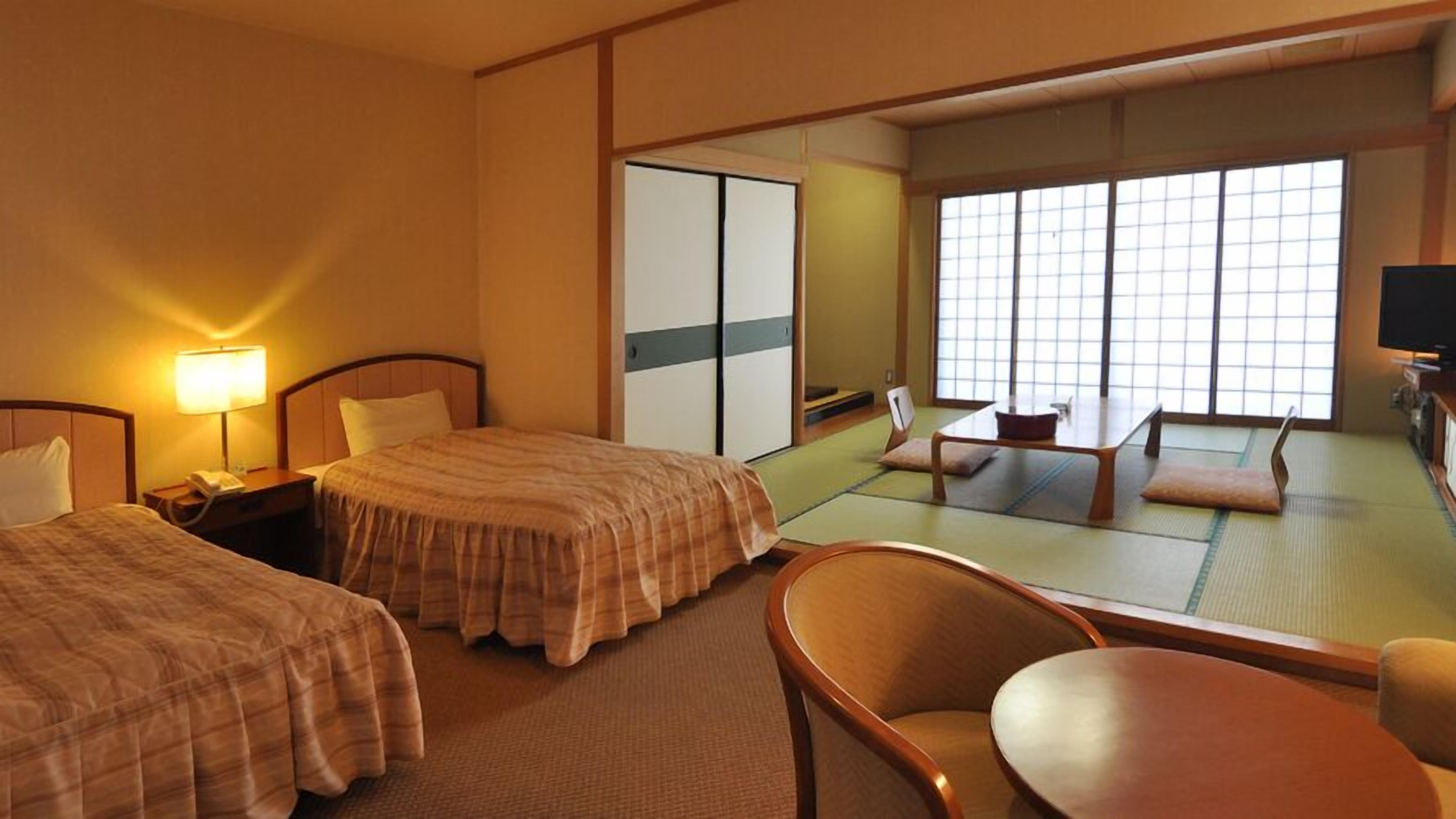 A hotel room with two beds, a desk, a chair, a TV, and a sliding door leading to a tatami mat room.