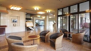 Een hal met rieten stoelen, een receptiebalie en een grote glazen deur naar buiten.