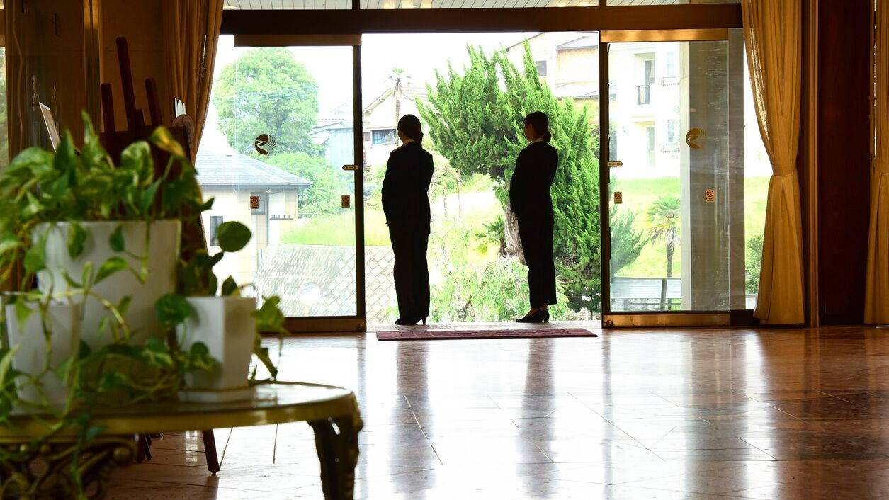 A hotel lobby with a large glass door, a potted plant, and a wooden floor.