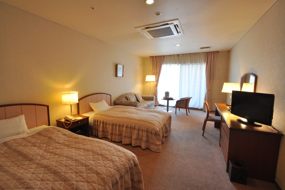 Ett hotellrum med två sängar, ett skrivbord med en tv, en stol och ett litet bord med en lampa.