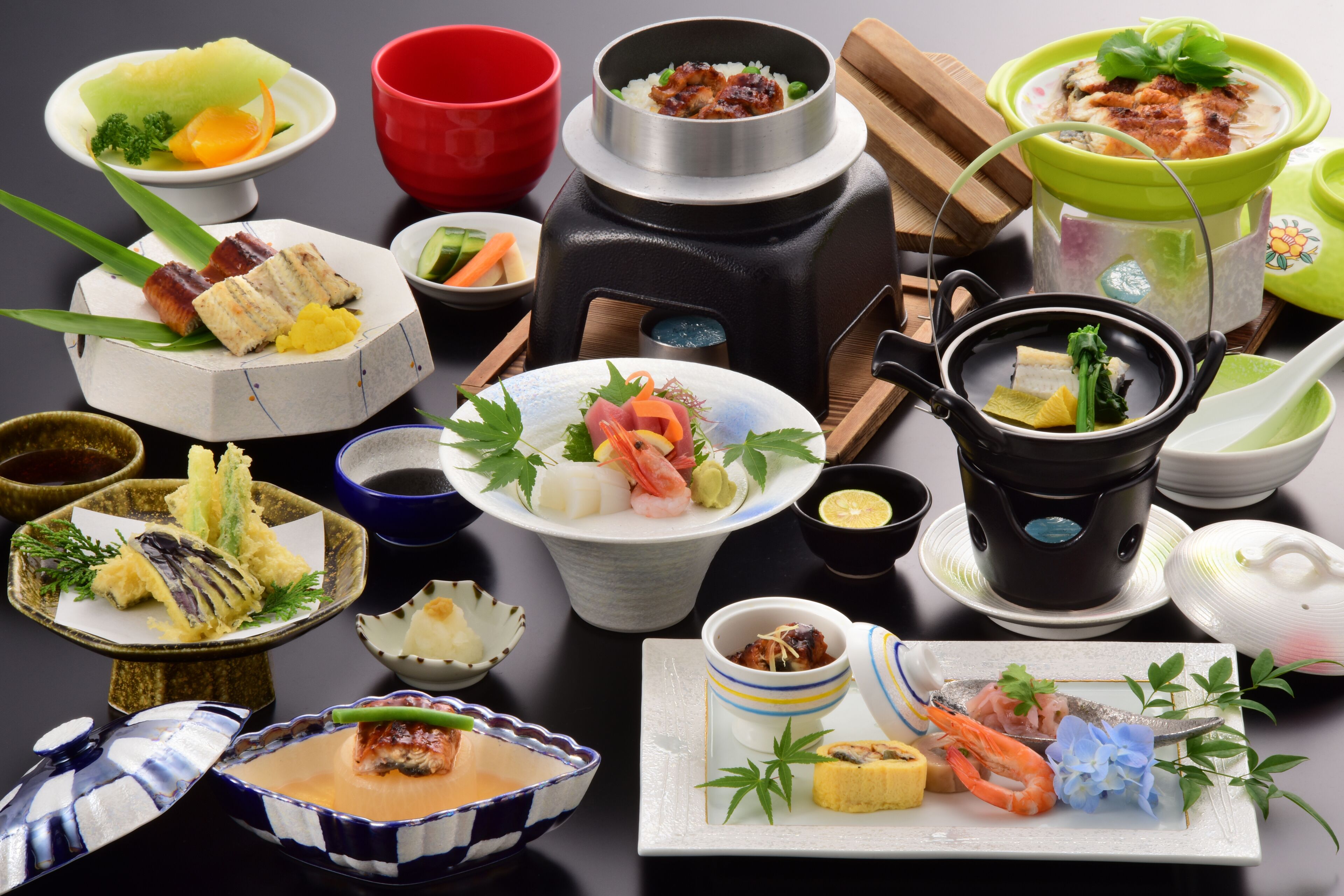 Diversos pratos japoneses dispostos sobre uma mesa, incluindo sushi, sashimi e outras iguarias, com tigelas e utensílios tradicionais.