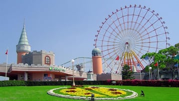 A large Ferris wheel, a castle-like building, and a circular flower bed with a statue in the foreground.