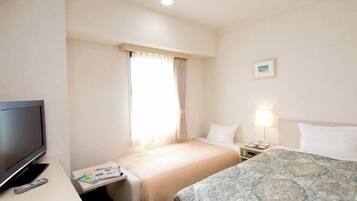 A hotel room with a bed, a TV, a bedside table with a lamp, and a window with curtains.