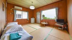 Une chambre avec un lit, une petite table, un téléviseur et une fenêtre avec des rideaux.