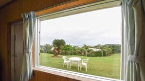 A room with a large window overlooking a grassy garden with a table and chairs. - Pension Hoshi NO Suna (Taketomi)