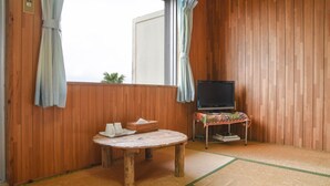 A wooden room with a tatami mat floor, a small table with a basket and cups, a television on a stand, and a window with curtains. - Pension Hoshi NO Suna (Taketomi)