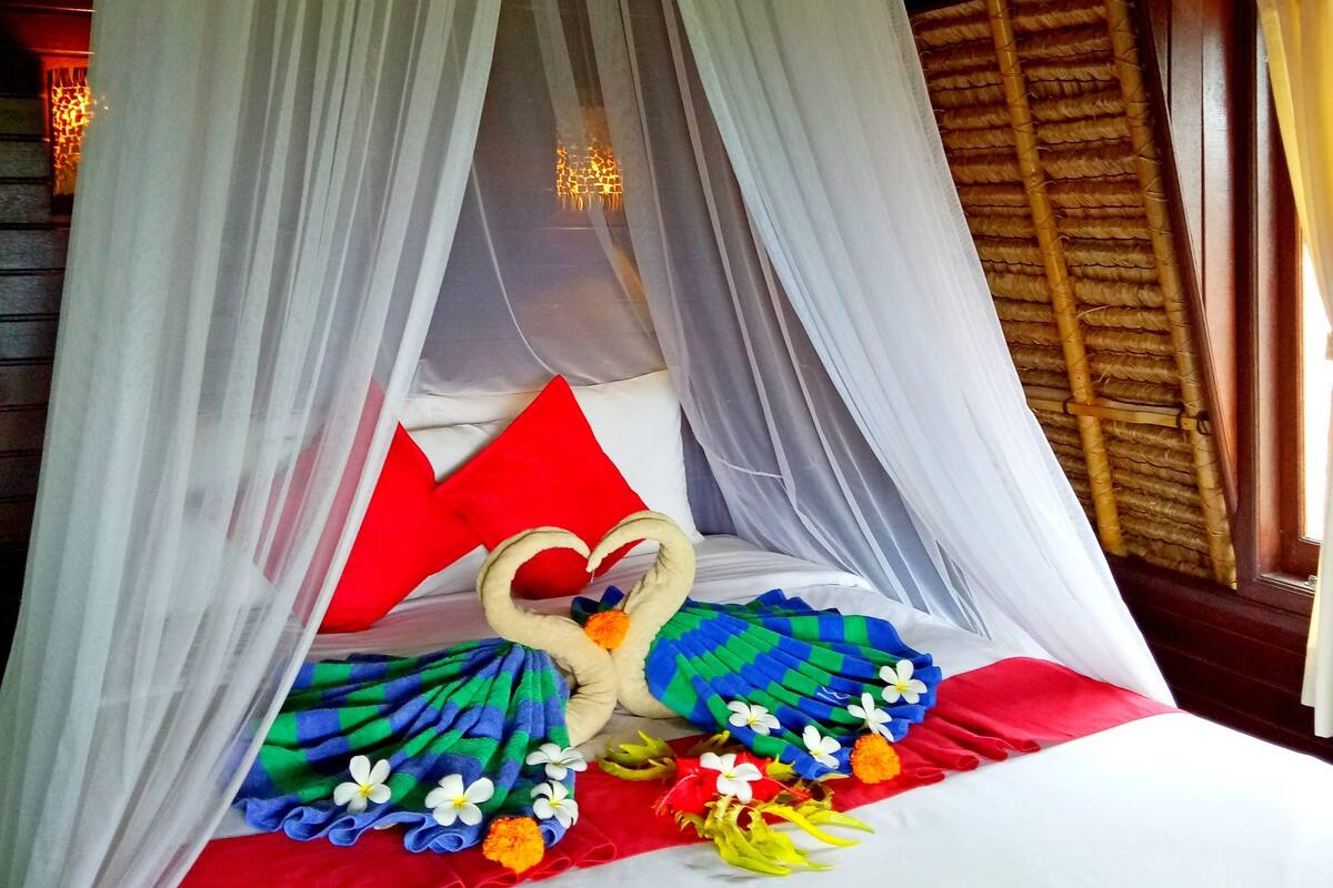 Un lit à baldaquin, avec des oreillers et un coussin décoratif en forme de cœur.