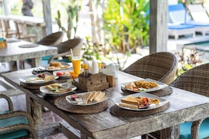 A wooden table with various dishes and condiments, surrounded by wicker chairs. - Dream Beach Kubu & Spa by ABM (Lembongan Island)