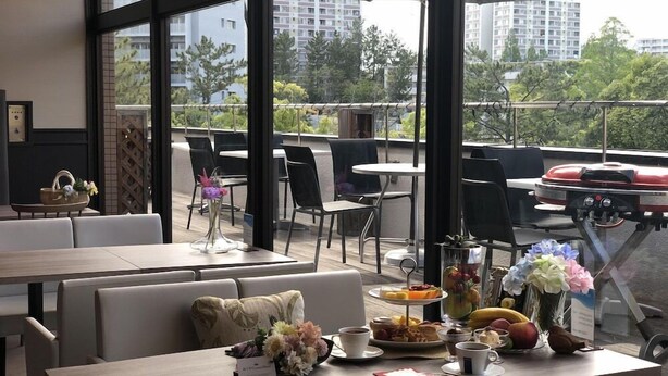 A modern outdoor dining area with tables and chairs, a buffet with fruits and pastries, and a view of the cityscape. - Crystal Hotel Minami Senri (Suita)