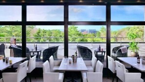 An outdoor dining area with tables and chairs, large windows, and a view of greenery and buildings. - Crystal Hotel Minami Senri (Suita)