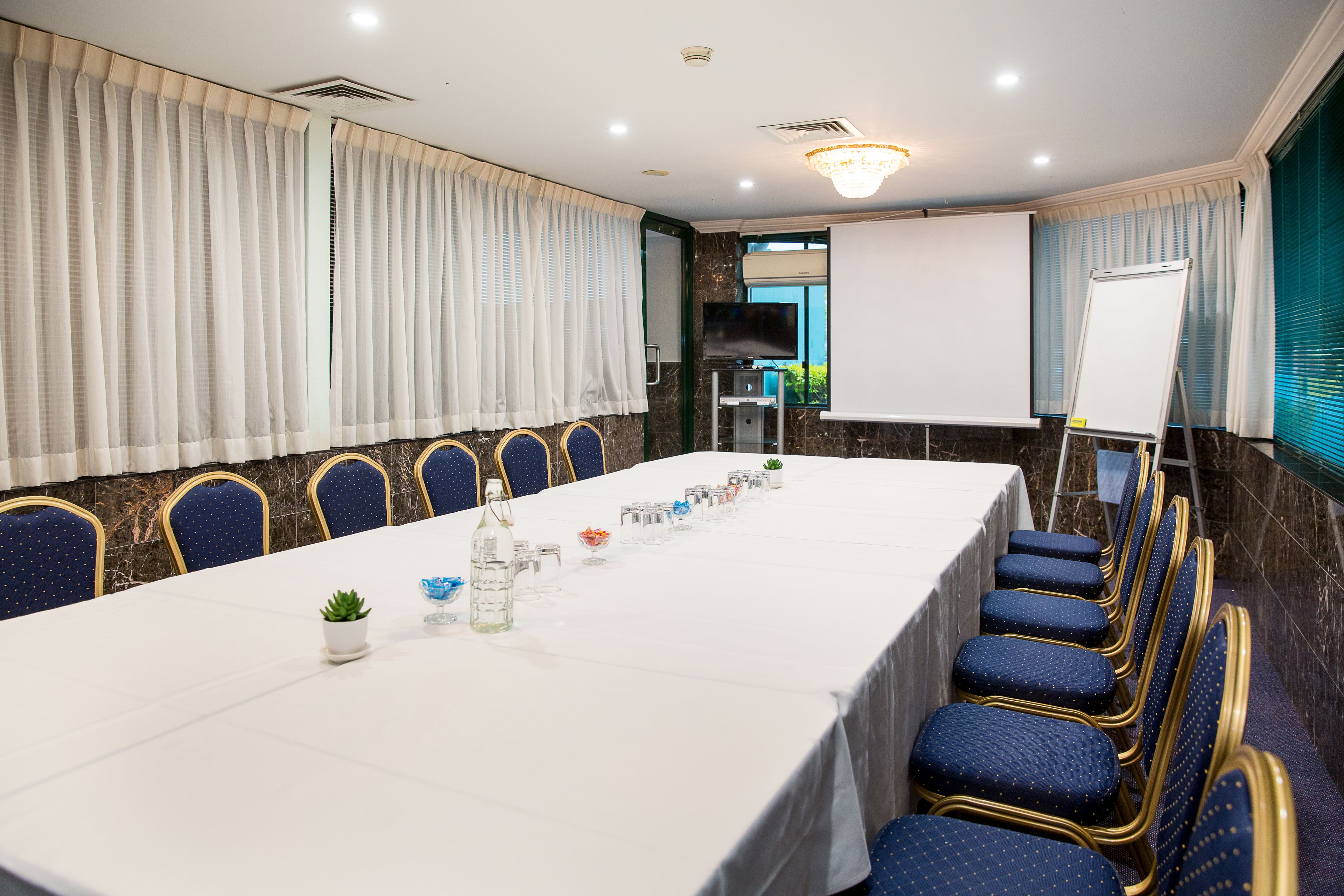 A conference room with a long table, blue chairs, a whiteboard, and a television.