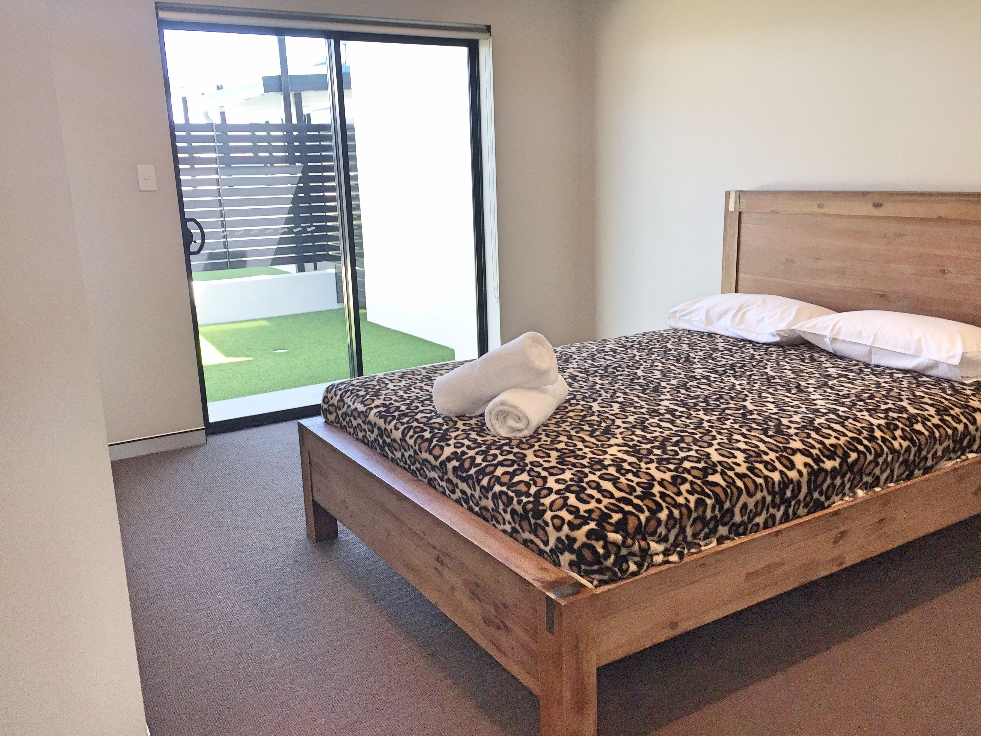 A bedroom with a wooden bed, a leopard print bedspread, white pillows, and a rolled towel on the bed.
