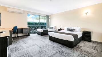 Ein Hotelzimmer mit einem großen Bett, einem Schreibtisch und einem Stuhl. Ein Fenster bietet Blick auf Grünfläche draußen.