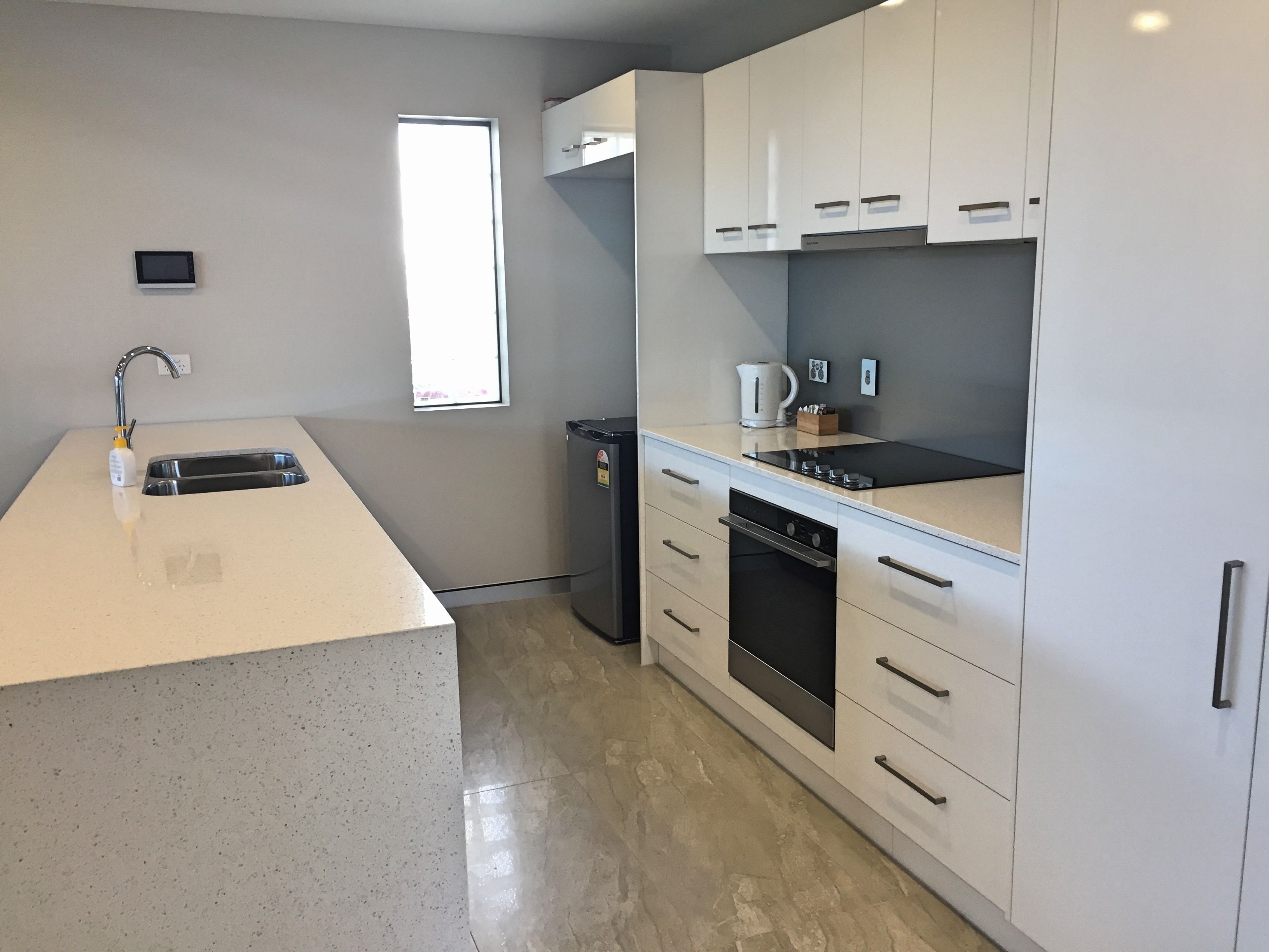 A modern kitchen with white cabinets, a stainless steel sink, a built-in oven, and a window providing natural light.