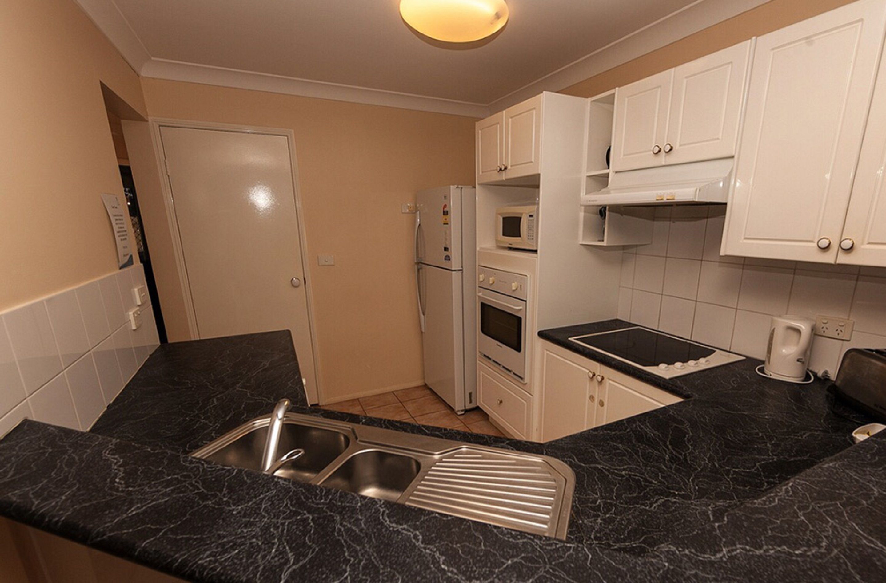 A compact kitchen with white cabinets, a black marble countertop, a built-in microwave, a stove, and a sink.